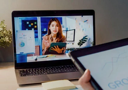 Someone views a video of another woman on her laptop screen while seated at a desk.